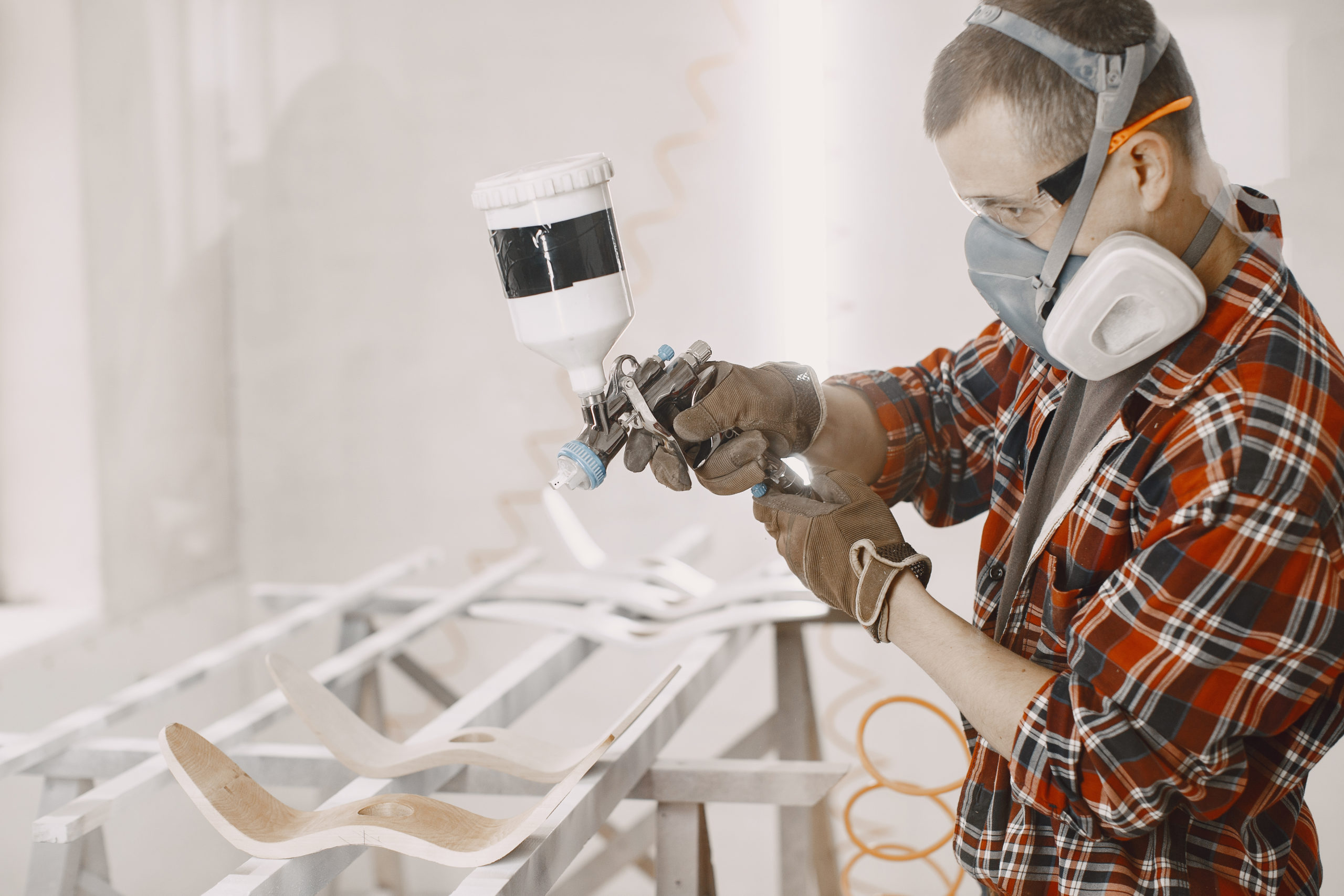 Yooung repairman carpenter working with paint painting. Master painter in a factory painting wood with spray gun.